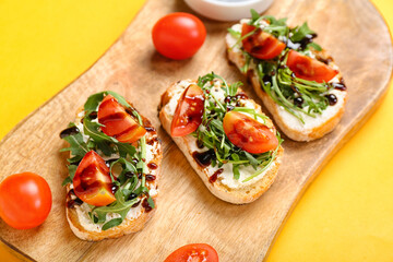 Fototapeta na wymiar Wooden board of tasty sandwiches with cream cheese, arugula and tomatoes on color background, closeup