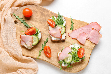 Wooden board of delicious sandwiches with cream cheese, ham and vegetables on light background, closeup
