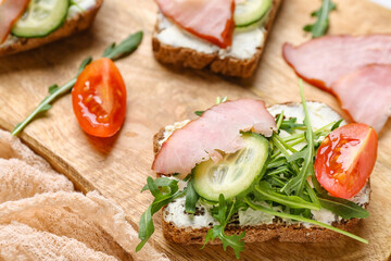 Wooden board of delicious sandwiches with cream cheese, ham and vegetables, closeup