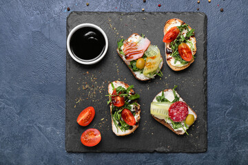 Slate board with tasty sandwiches and sauce on dark background