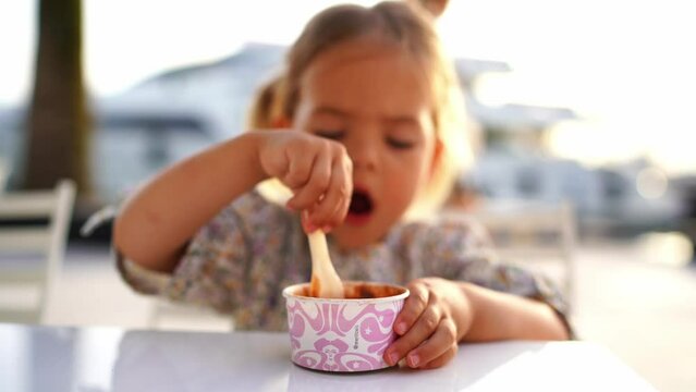 Little girl stirs chocolate ice cream in a cup with a spatula