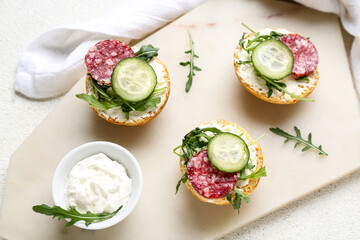 Board with delicious sandwiches and cream cheese on light background, closeup