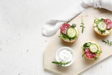 Board with delicious sandwiches and cream cheese on light background