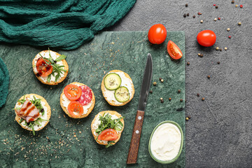 Board with tasty sandwiches, cream cheese, tomatoes and spices on dark background