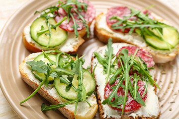 Plate of tasty sandwiches with cream cheese, cucumber, arugula and salami, closeup