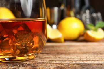 Glass of rum with ice cubes on wooden background, closeup