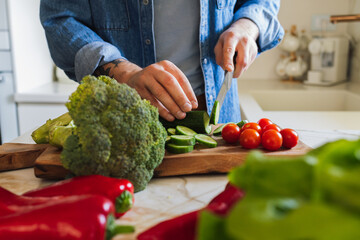Close-up photo of a man cutting vegetables (cucumber, cherry tomato, broccoli) on a wooden board