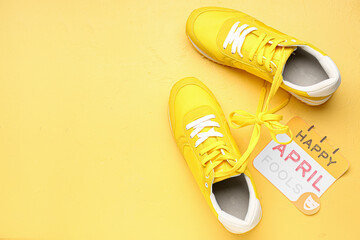 Paper with text HAPPY APRIL FOOLS and sneakers on yellow background