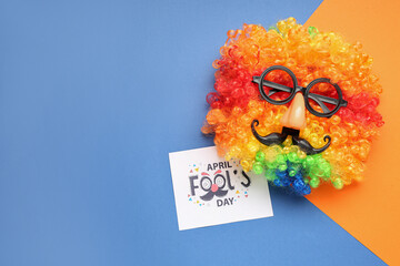 Paper with text APRIL FOOL'S DAY, clown wig and funny disguise on color background