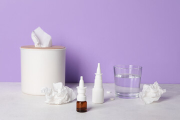 Bottles of drops with tissue box and water on table near lilac wall. Allergy concept