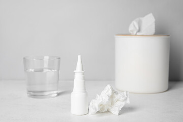 Fototapeta na wymiar Nasal drops with tissue box and glass of water on table near grey wall. Allergy concept