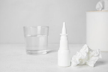 Nasal drops with tissue and glass of water on table near grey wall, closeup. Allergy concept