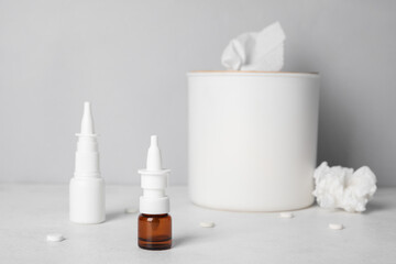 Bottles of drops with pills and tissue box on table near grey wall. Allergy concept