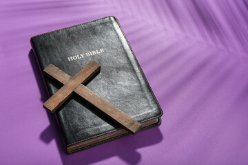 Wooden cross with Holy Bible on violet background. Good Friday concept