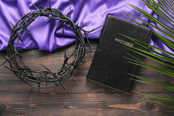 Holy Bible with palm leaf, crown of thorns and purple fabric on wooden background. Good Friday...