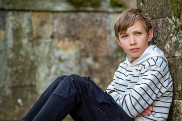 Teen boy sitting outside alone and looking into the distance. Sad kid in a park glancing away....
