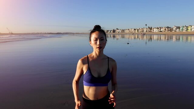Athletic Asian woman jogging on the beach in Southern California. Slow motion.