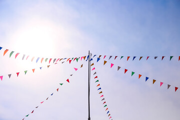 Many flags paper hang on white string line and pole on bright blue sky background