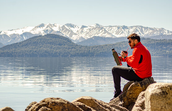chico hombre persona a la orilla del lago rodeado de monta&ntilde;as mirando el paisaje tomando mate argentino  