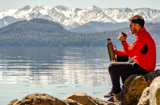 chico hombre persona a la orilla del lago rodeado de monta&ntilde;as tomando su mate argentino 