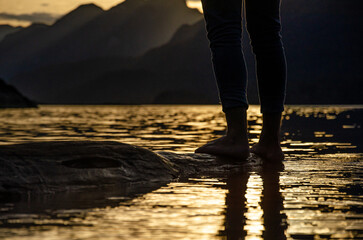 pies de una persona sobre un árbol al borde del agua de un lago en la Patagonia Argentina al atardecer con montañas de fondo