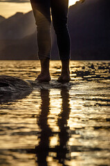 pies de una persona sobre un árbol al borde del agua de un lago en la Patagonia Argentina al atardecer con montañas de fondo