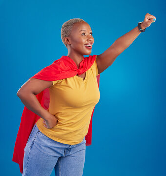 Black Woman, Superhero Cape And Flying In Studio, Blue Background And Pop Culture Fashion. Happy Female Model, Cosplay Character And Superwoman Costume Of Fist, Courage Or Action Of Strong Girl Power