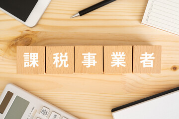 課税事業者と書かれたブロック、電卓、スマホ、ノート、カレンダー