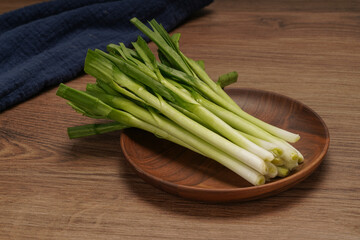 A pile of green onions on a wooden plate