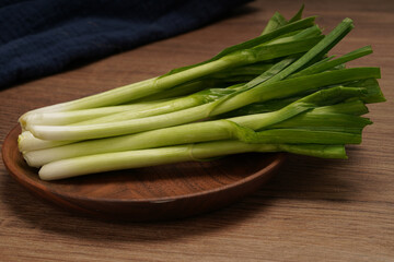 A pile of green onions on a wooden plate