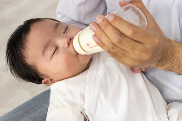 父親に抱っこされて寝ながらミルク飲む赤ちゃん（0歳3か月、日本人、男の子） - obrazy, fototapety, plakaty