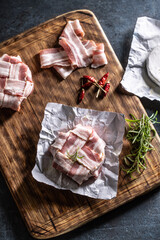 Top view of camembert cheese wrapped in slices of bacon along with chilli and rosemary