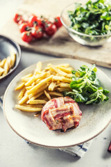 Round cheese wrap in prosciutto served with fries, salad and cherry tomatoes