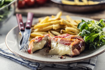 Cut melting cheese in a bacon wrap served on a plate with french fries and green salad