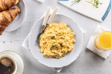 Top view of a breakfast menu consisting of yellow scrambled eggs, coffee, croissants and orange juice