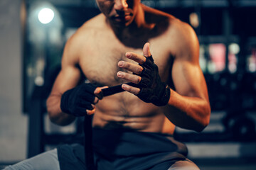Fototapeta na wymiar Athlete bodybuilder wearing sport gloves on hand for preparing exercise at gym. Asian man athlete shirtless in fitness gym. Weight training exercise in concept of health and wellness.