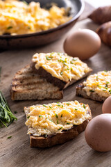 Toasts of bread with generous portion of scrambled eggs on top of it, sprinked with freshly chopped chives