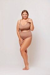 Pretty plus size female model dressed in nude bodysuit isolated on light background, stands with a...