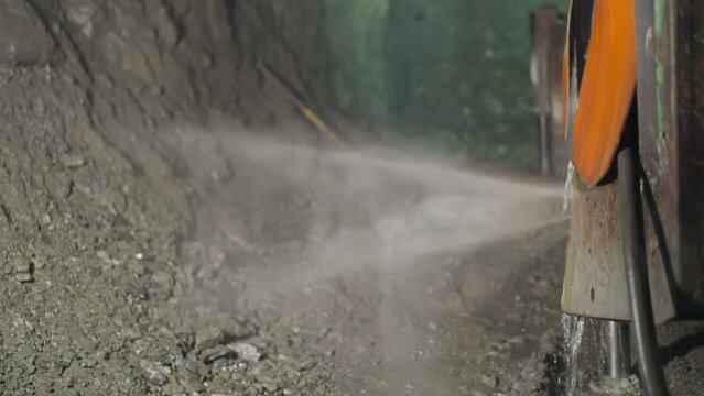 Heavy machinery equipment with coolant and robot drill operates in ore mine. Cold water sprayed to cool soil during rock drilling process closeup