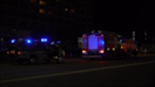 Background, blurred image of fire trucks with blue flashing beacons turned on, arriving at the scene at night.