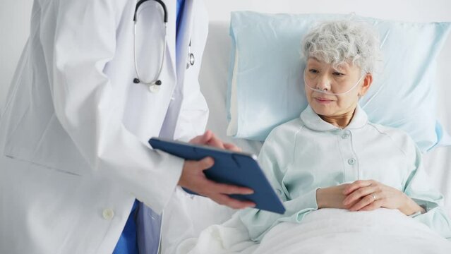 高齢の入院患者にタブレットで症状を説明する医師