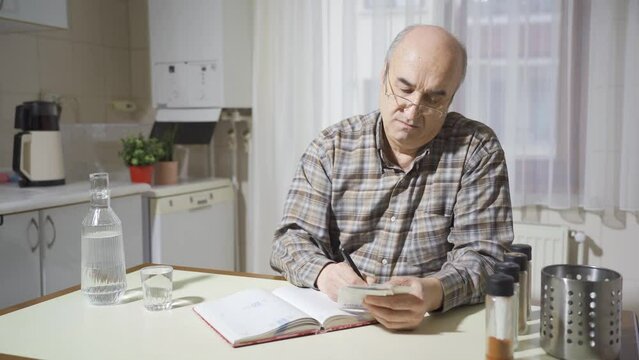 Old man looking at bills calculating at home. 
Retired man trying to pay bills, high bills bother him.

