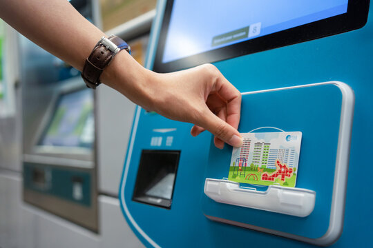 SINGAPORE - APR 19, 2022: Lady's hand placing the Singapore MRT Card (EZ-Link) at the card reader area of the ticket machine. Passenger reload EZ-Link Card using Ticket vending machine.