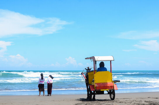 Tourists and Dokar standing on the shore of Parangtritis Beach, Yogyakarta, Indonesia. Dokar is a traditional means of transportation pulled by a horse.