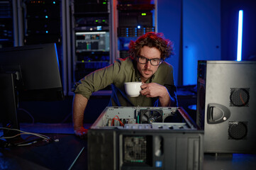 Fototapeta na wymiar Repairman with cup of coffee looking at disassembled computer system unit
