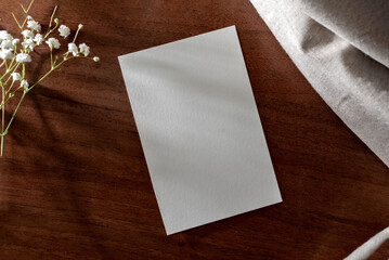 Blank paper card with floral shadows on dark brown table surface background, minimalist classic...