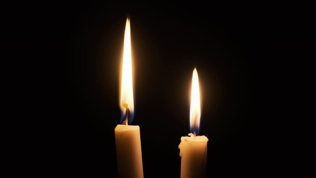 Two candle burns on a black background. Close-up of a yellow flickering flame illuminates the darkness. Isolated, Copyscape. The warm glow of flame moving with the soft wind at night. 4K