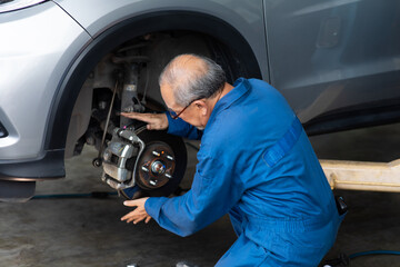 Fototapeta na wymiar Asian senior man mechanic changing car wheel at Car maintenance and auto service garage. Elderly male worker people