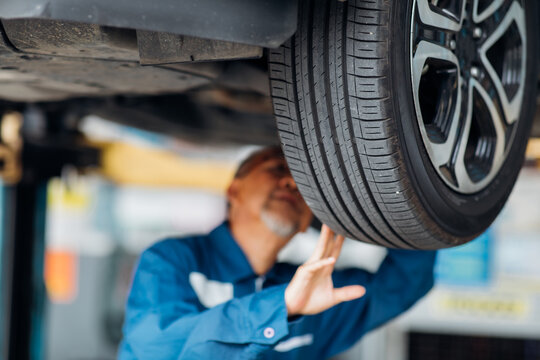 Asian senior man mechanic changing car wheel at Car maintenance and auto service garage. Elderly male worker people - Powered by Adobe