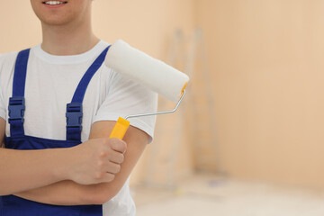 Worker holding paint roller in unfinished room, closeup. Space for text